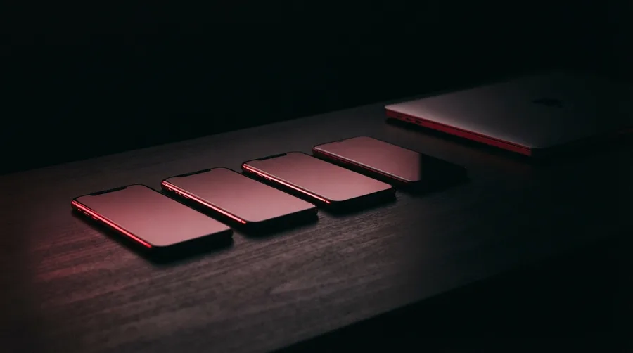 Varios celulares sobre un escritorio oscuro con las pantallas iluminadas en rojo.